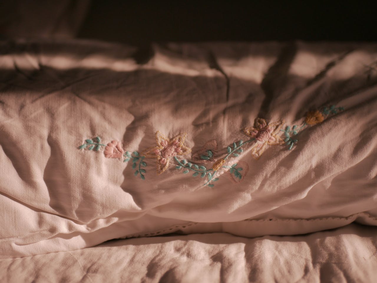 Close-up of delicate floral embroidery on a soft pink pillowcase, showcasing elegance.