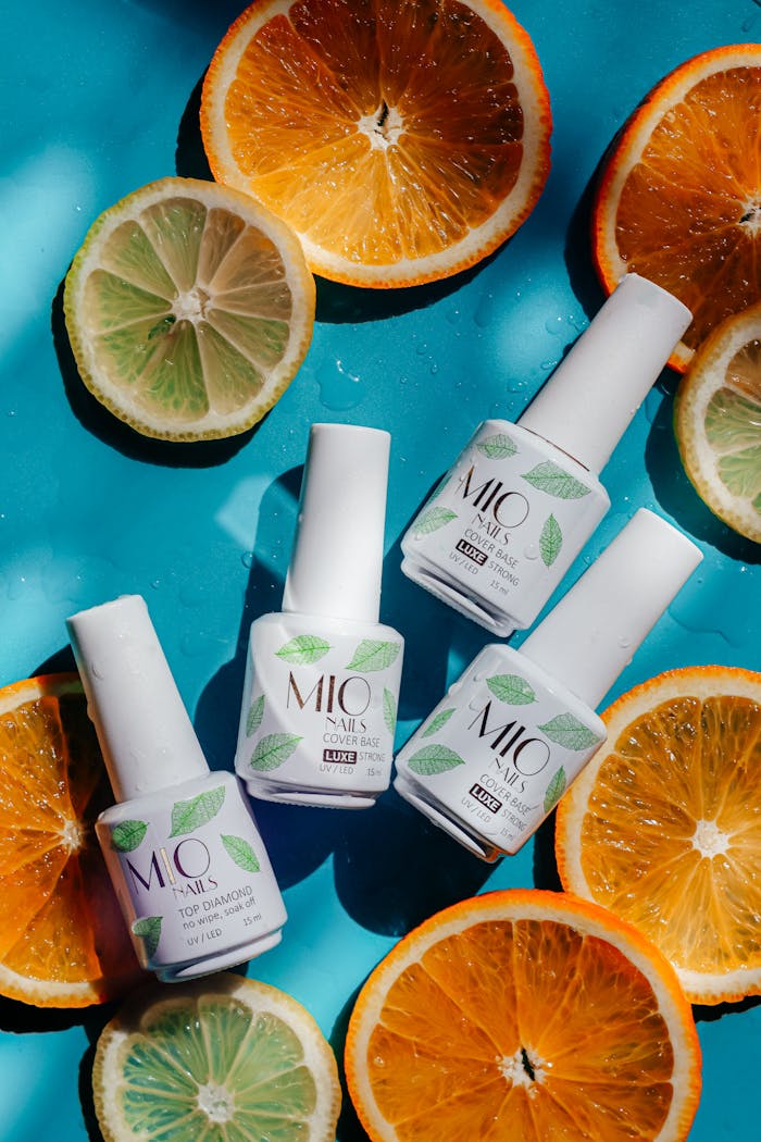 A colorful flatlay of nail polish bottles surrounded by fresh citrus slices on a blue background.